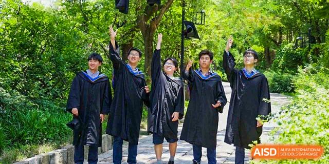 Three graduating students from Yew Wah International Education School of Zhejiang Tongxiang in caps and gowns celebrating outdoors.