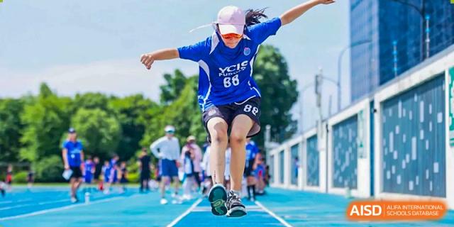 A female student from Yew Wah International Education School of Zhejiang Tongxiang in a blue athletic uniform jumping on a blue running track during a sports event.