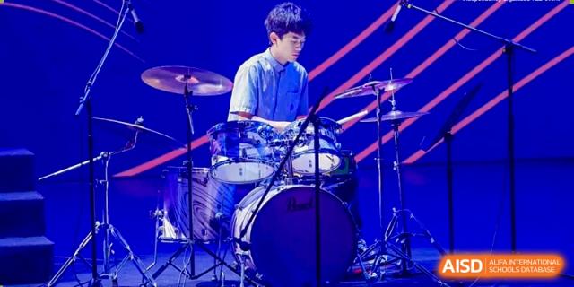 A male student from Yew Wah International Education School of Zhejiang Tongxiang playing the drums during a performance.