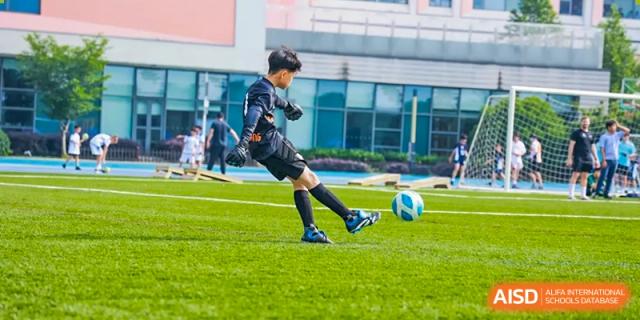 A student from Yew Wah International Education School of Zhejiang Tongxiang kicking a soccer ball on a green sports pitch.
