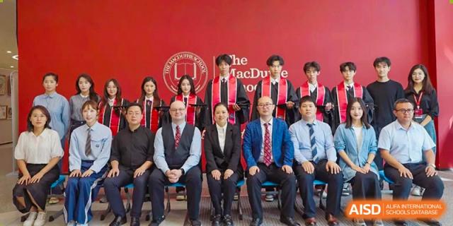 A formal group portrait of school leaders, teachers, and students seated and standing in front of a red backdrop with the school logo at Zibo MacDuffie Bilingual High School.