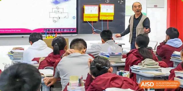 A teacher demonstrating an experiment with wiring and meters on a smart board to a small group of students in a classroom at Zibo MacDuffie Bilingual High School.