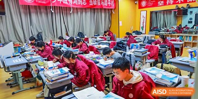 A close-up view of students in red uniforms intently focused on their work or exams in a busy classroom setting at Zibo MacDuffie Bilingual High School.