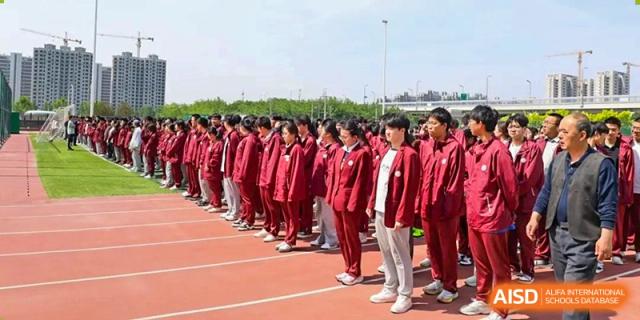 A large group of students in matching red and white school uniforms lined up on a track during an outdoor event at Zibo MacDuffie Bilingual High School.