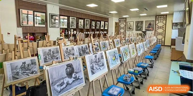 A brightly lit art room with numerous easels displaying various pencil and charcoal sketches, with framed artwork on the back wall at Zibo MacDuffie Bilingual High School.