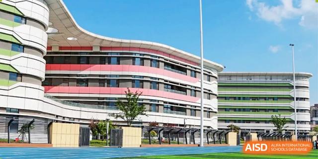 An exterior view of the main school building, a large modern structure with red and white accents, at Zibo MacDuffie Bilingual High School.