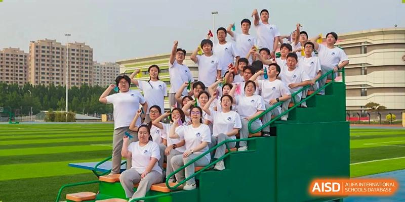 A large group of students in white shirts cheering excitedly in stadium seating at Zibo MacDuffie Bilingual High School.