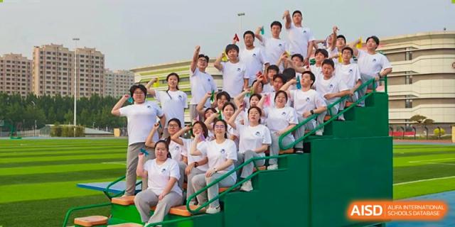 A large group of students in white shirts cheering excitedly in stadium seating at Zibo MacDuffie Bilingual High School.