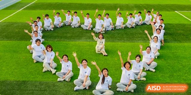 A group of female students sitting on the grass, waving and smiling, during an outdoor activity at Zibo MacDuffie Bilingual High School.
