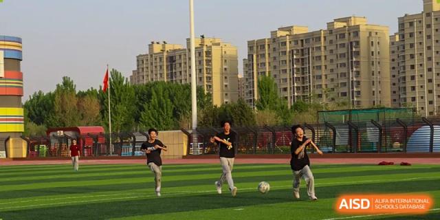 Students playing soccer or football on an outdoor field with apartment buildings in the background at Zibo MacDuffie Bilingual High School.