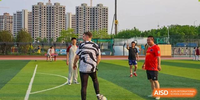 Students playing on a green turf field, with one student facing away in a patterned shirt, at Zibo MacDuffie Bilingual High School.