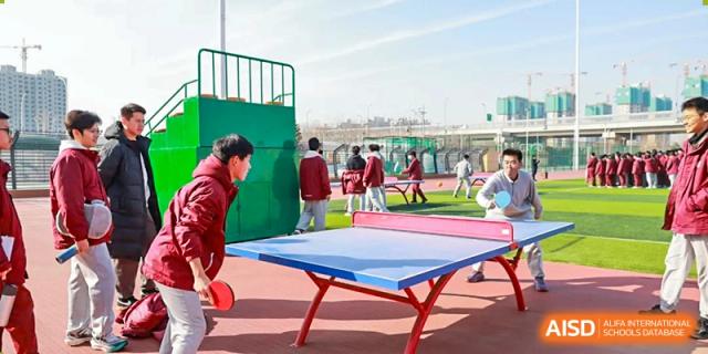 An outdoor sports area with a blue table tennis table and students in the background at Zibo MacDuffie Bilingual High School.