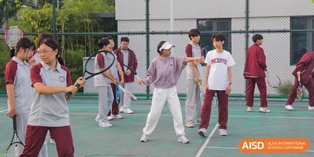 A female student in light pants playing table tennis or a similar racket sport outdoors at Zibo MacDuffie Bilingual High School.