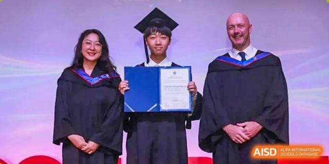 A graduate from Yew Wah International Education School of Yantai Campus in a cap and gown holding a diploma at the closing ceremony.