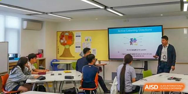 Yew Wah International Education School of Yantai Campus students attending a lesson in a classroom with a bright yellow wall and a large screen display.