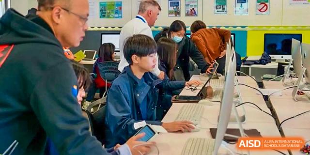 Yew Wah International Education School of Yantai Campus students working on laptops and tablets in a classroom setting.