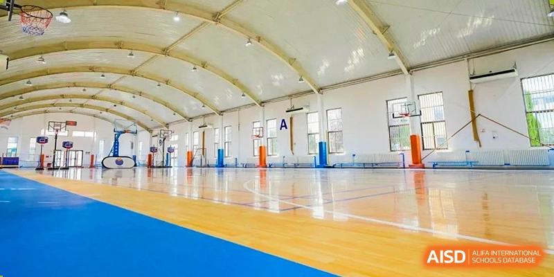 An empty indoor gymnasium with a polished wooden floor and basketball hoops at Yew Wah International Education School of Yantai Campus.