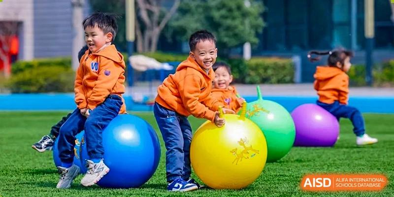Two young children from Yew Wah International Education School of Yantai Campus playing happily with large colorful exercise balls outdoors.