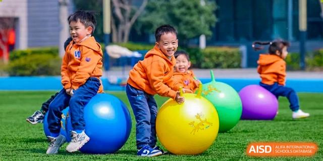 Two young children from Yew Wah International Education School of Yantai Campus playing happily with large colorful exercise balls outdoors.