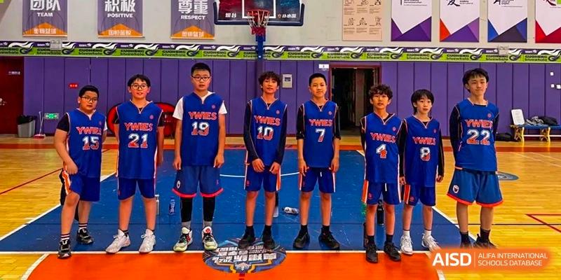 A basketball team from Yew Wah International Education School of Yantai Campus in blue jerseys posing for a photo on the court.