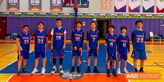 A basketball team from Yew Wah International Education School of Yantai Campus in blue jerseys posing for a photo on the court.