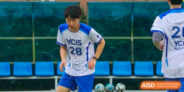 A Yew Wah International Education School of Yantai Campus student in a white and blue sports uniform (YCIS 28) preparing for a football (soccer) game.