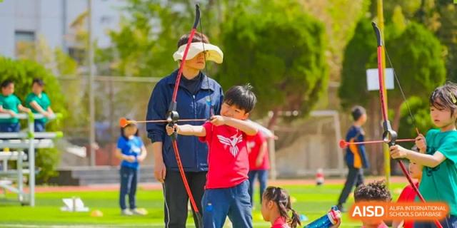 An archery instructor guiding a student from Yew Wah International Education School of Yantai Campus at an outdoor activity.