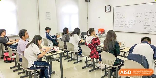 Students seated at their desks in a classroom, actively writing or working on assignments during an in-class session, at Ulink College of Beijing.