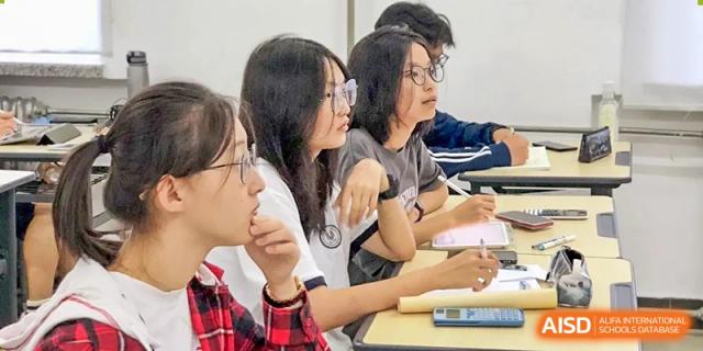 A group of students sitting closely together at a desk, engaged in a discussion or collaborative activity in a classroom, at Ulink College of Beijing.