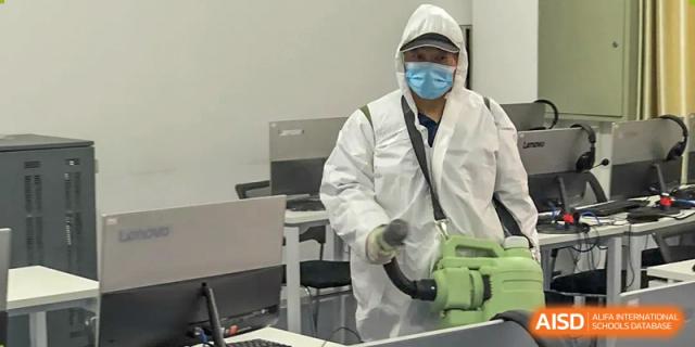 A school staff member wearing full protective personal equipment (PPE) and a face shield, likely for health and safety, at Ulink College of Beijing.