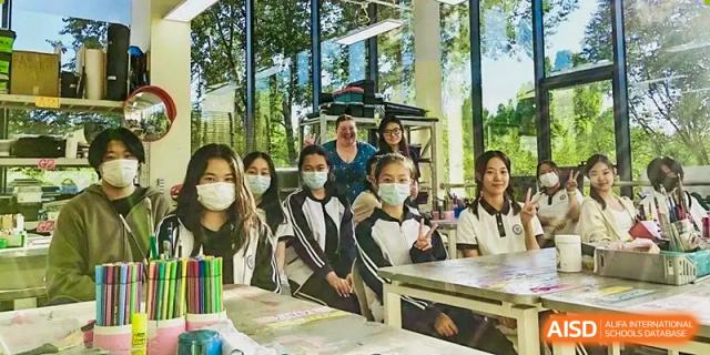 A group of smiling students wearing protective masks, standing together in a brightly lit indoor space, at Ulink College of Beijing.