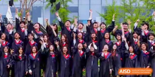 A group of students in graduation gowns cheering enthusiastically with their hands raised outside the school building, at Ulink College of Beijing.