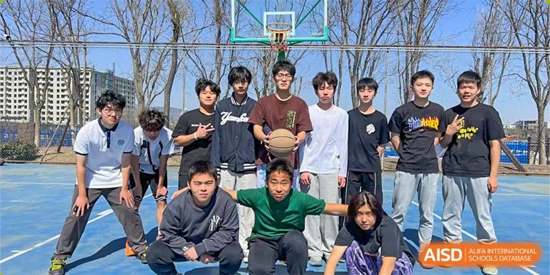 A group of male and female students posing together on an outdoor basketball court, with one student holding a basketball, at Ulink College of Beijing.