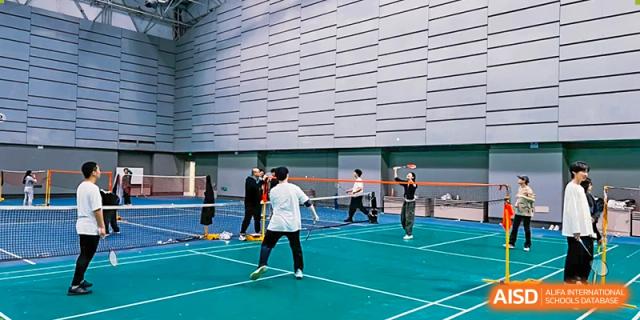 A student playing a racket sport, possibly badminton or tennis, on an outdoor blue court next to a modern building, at Ulink College of Beijing.