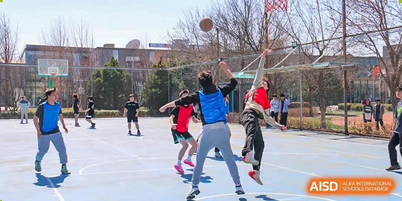 Students playing an outdoor basketball or volleyball game, with one student jumping up to shoot the ball, at Ulink College of Beijing.