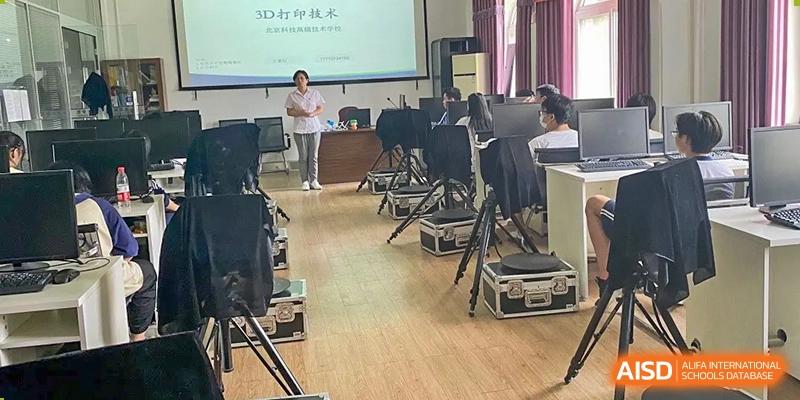 An indoor classroom or lecture hall with a teacher presenting at the front, with rows of empty chairs facing the screen, at Ulink College of Beijing.