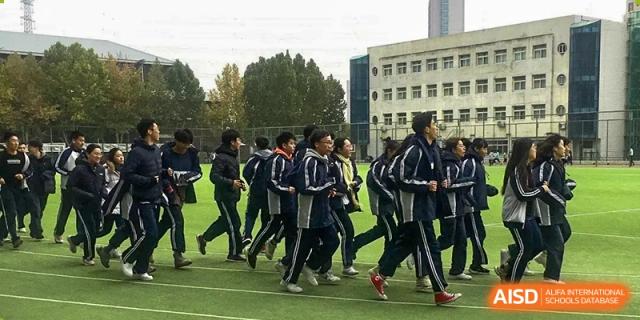 A group of male students in dark uniforms running together on a sports field during an athletic training session, at Ulink College of Beijing.
