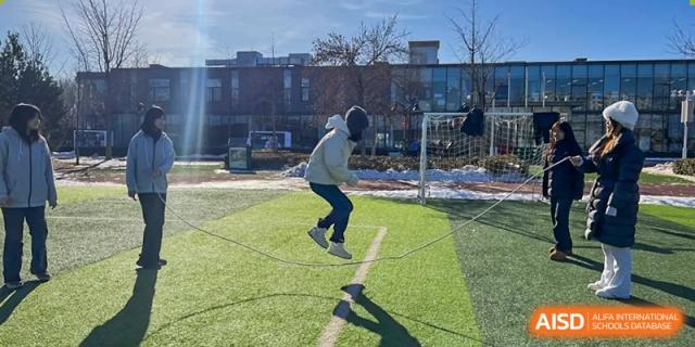 A student jumping across marked squares on the grass during an outdoor fitness or sports training activity on a cold day, at Ulink College of Beijing.