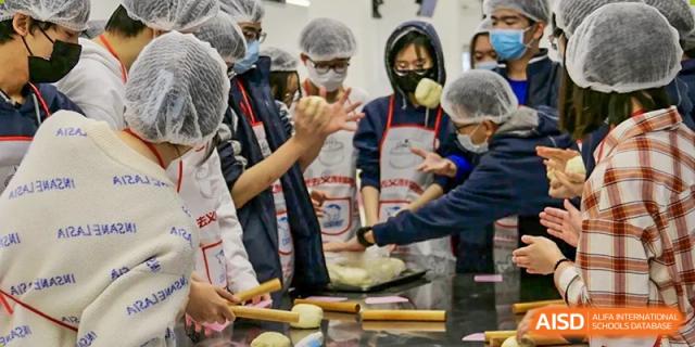 A student wearing an apron, gloves, and a face mask is learning to prepare food or bake during a hands-on culinary class, at Ulink College of Beijing.