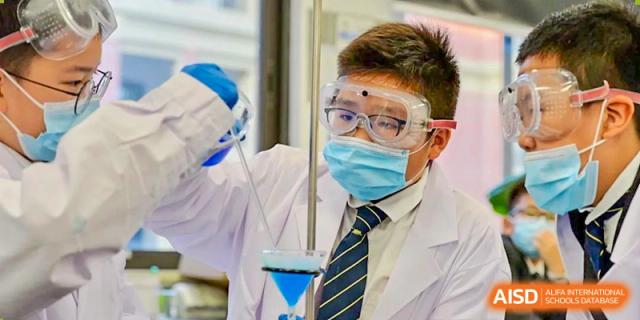 A student wearing safety goggles, a mask, and a lab coat conducts an experiment with glassware in a science lab at Sedbergh School Fuzhou.
