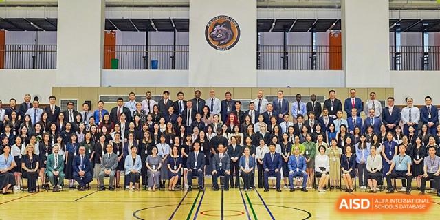 Large group photo of students, teachers, and administrators posing for a formal portrait in a gymnasium with Sedbergh School Fuzhou banner visible on the wall.