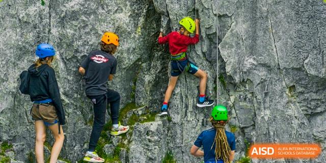 Students wearing helmets and safety harnesses rock climbing outdoors on a natural-looking cliff face, showcasing an adventure sport activity at Sedbergh School Fuzhou.