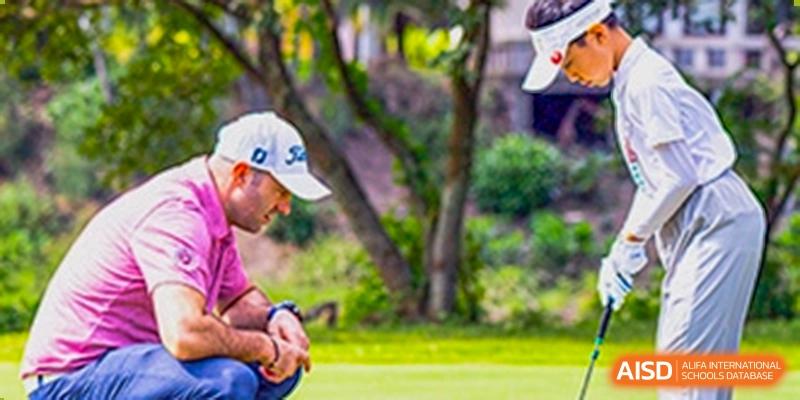 A man wearing a white cap kneels outdoors on a grassy area, possibly coaching or observing a sport or event at Sedbergh School Fuzhou.