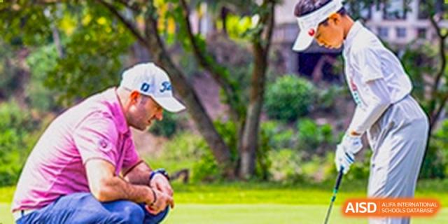 A man wearing a white cap kneels outdoors on a grassy area, possibly coaching or observing a sport or event at Sedbergh School Fuzhou.