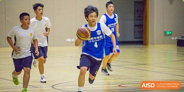 A student in a blue and white uniform dribbles a basketball aggressively down the court during a game at the indoor gym of Sedbergh School Fuzhou.