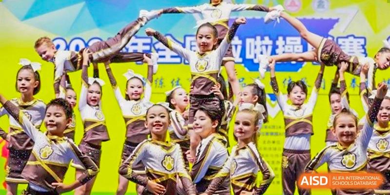 A group of smiling, energetic young students performing a synchronized dance or cheerleading routine at Sedbergh School Fuzhou.