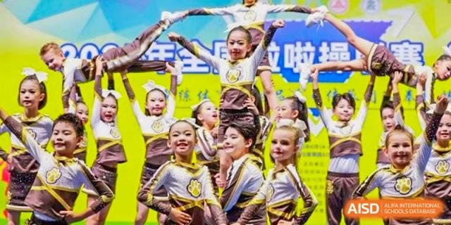 A group of smiling, energetic young students performing a synchronized dance or cheerleading routine at Sedbergh School Fuzhou.