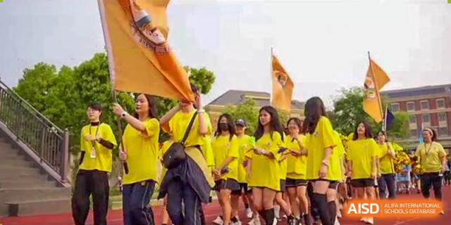 A group of female students in yellow shirts holding large flags and banners during an outdoor event or sports day at Sedbergh School Fuzhou.
