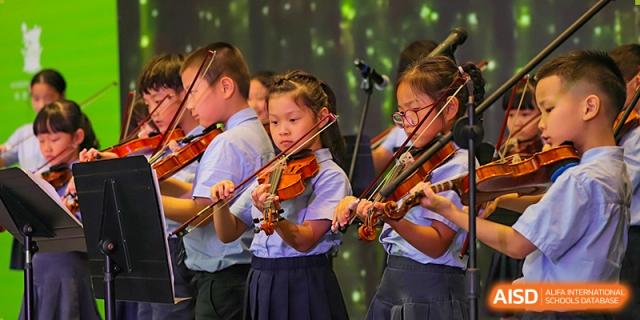 Primary students in school uniforms concentrating while playing violins together during a musical performance on stage at Sedbergh School Fuzhou.