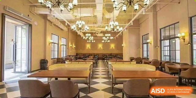 Interior view of a modern, well-lit school dining hall or cafeteria with wooden tables, benches, and chandeliers at Sedbergh School Fuzhou.